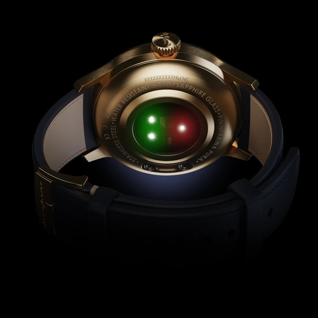Gold-cased Pininfarina Pura hybrid smartwatch by Globics, showing the optical heart-rate sensor glowing green and red on the sapphire caseback, with a navy leather strap on a black background