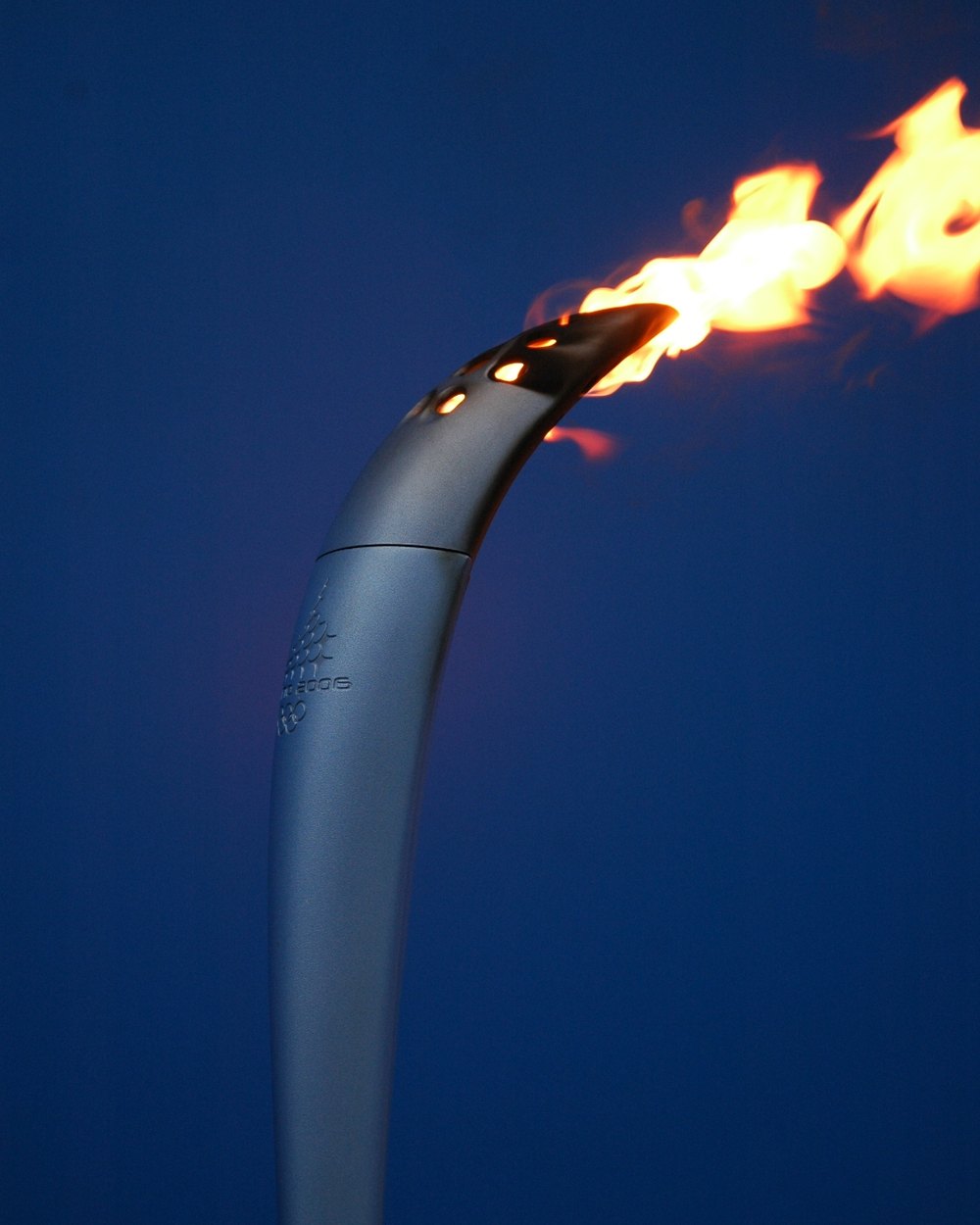 The 2006 Winter Olympic torch designed by Pininfarina, a sculpted silver form with a flame against a deep blue sky